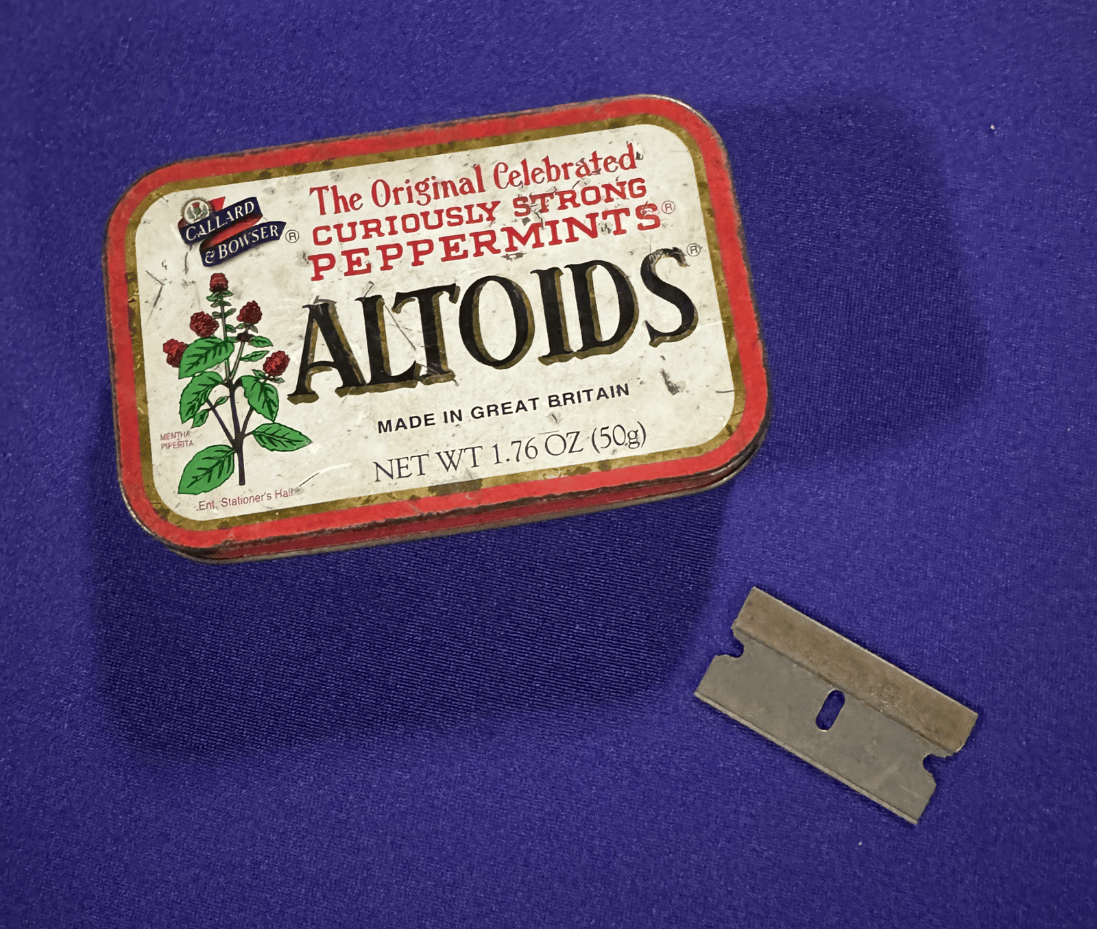 Old Altoids Tin and Razor Blade on Purple Felt Background